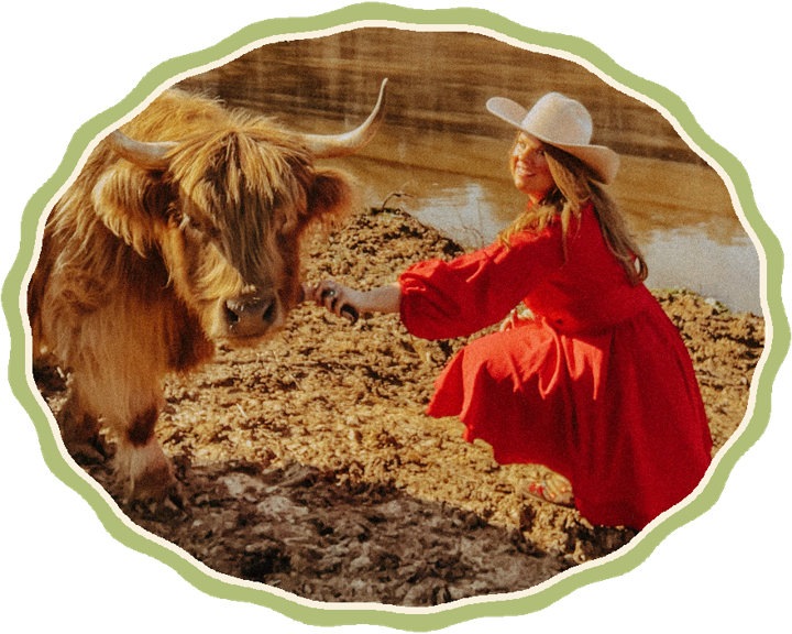 The author in a red dress smiling beside a Highland cow at the pond